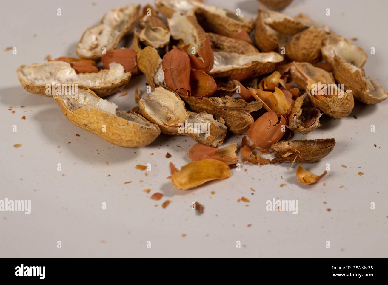 Nahaufnahme von leeren Erdnussschalen über einer weißen quadratischen Platte. Erdnussschale. Stockfoto