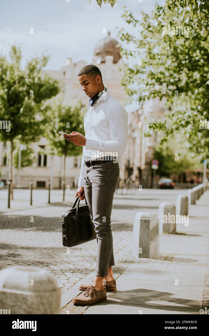 Hübscher junger afroamerikanischer Geschäftsmann, der ein Mobiltelefon benutzt Warten Sie auf ein Taxi auf einer Straße Stockfoto
