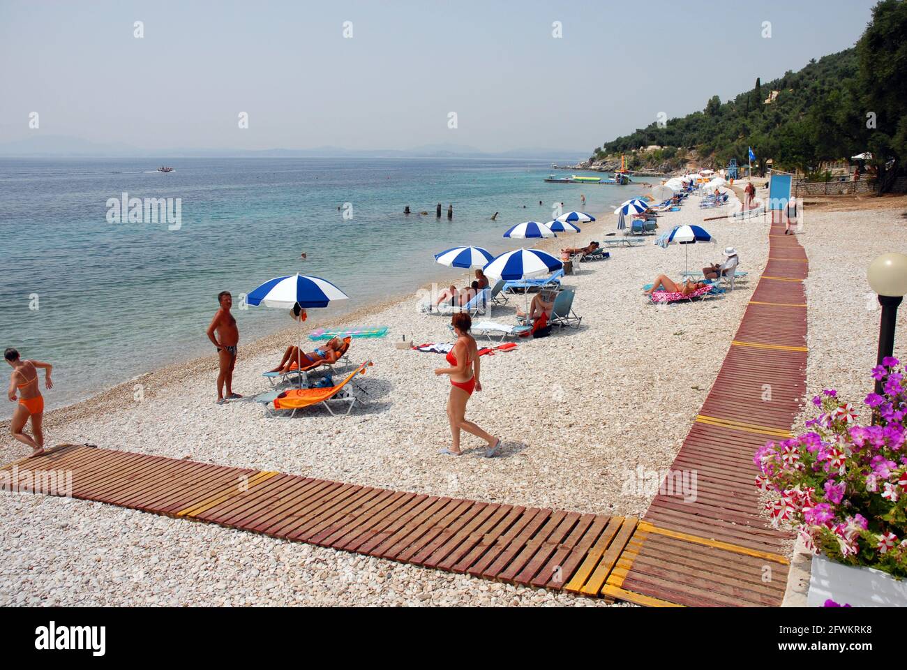 Leute zur freien Verfügung, genießen die heiße Sonne, Nissaki Beach, der mit zweckbestimmten hölzernen Gehwegen über dem Schindel versehen wird, Korfu, Griechenland Stockfoto