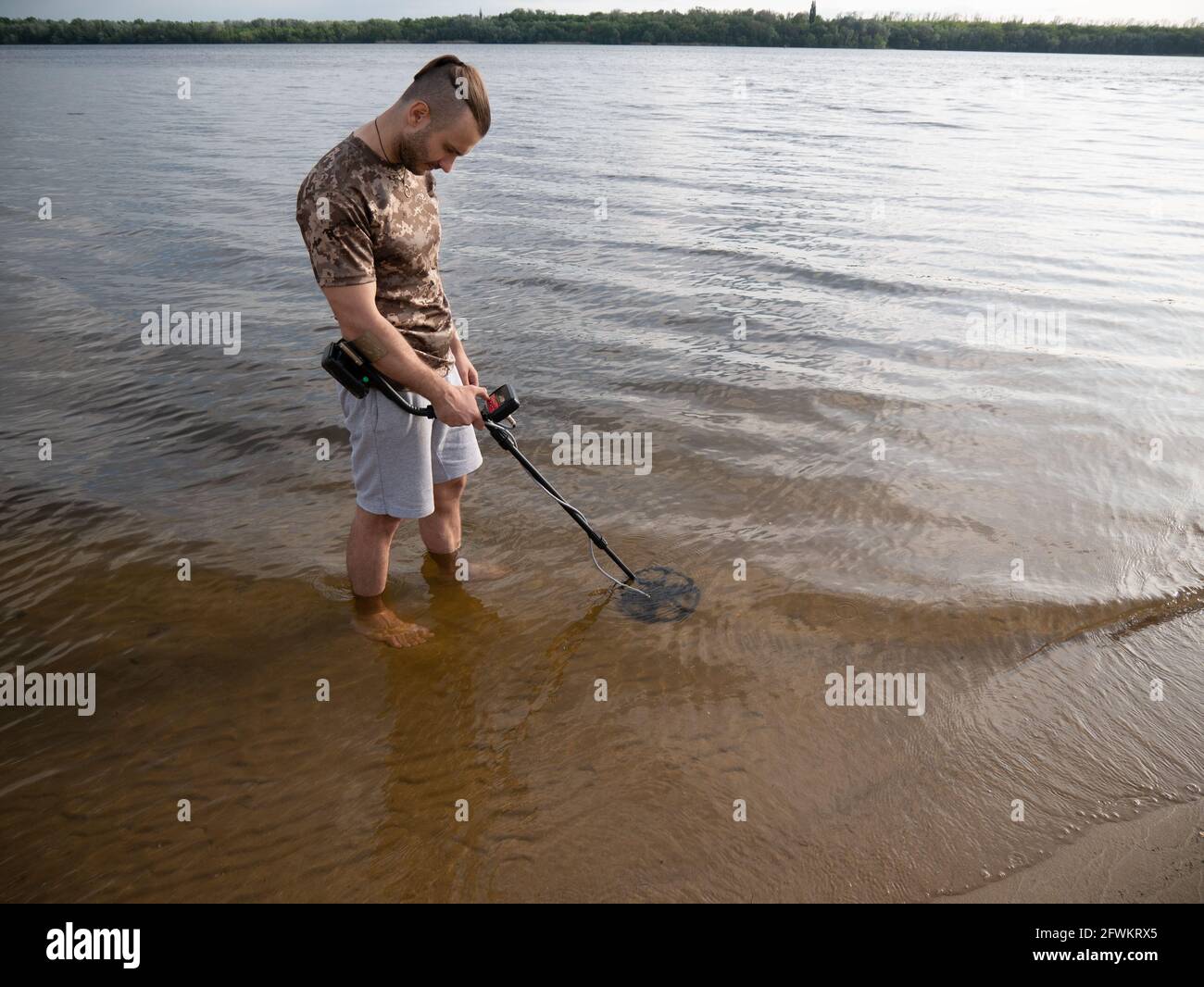 Der Typ im Fluss sucht einen Schatz mit einem Metalldetektor im Wasser. Stockfoto