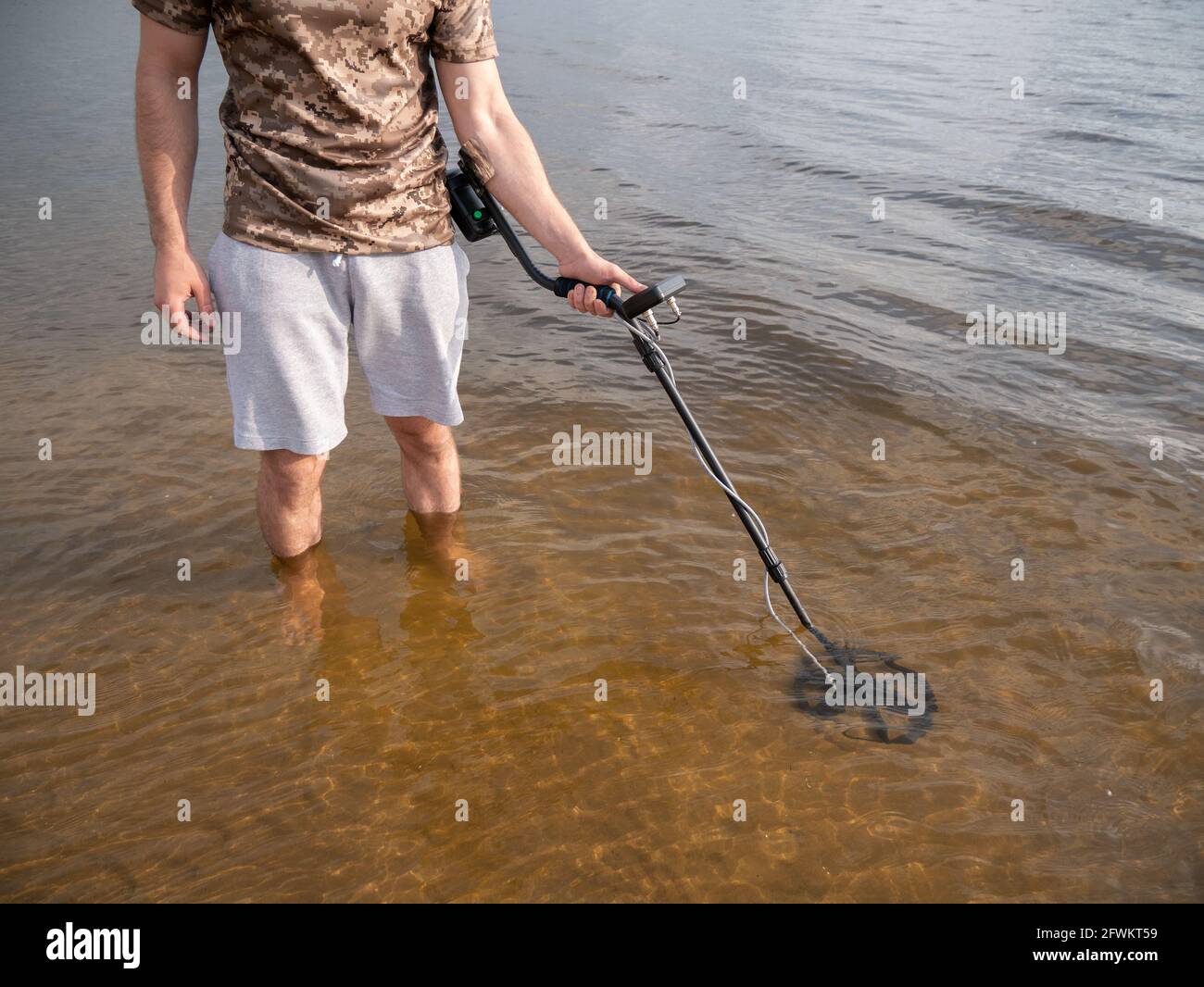 Der Typ im Fluss sucht einen Schatz mit einem Metalldetektor im Wasser. Stockfoto