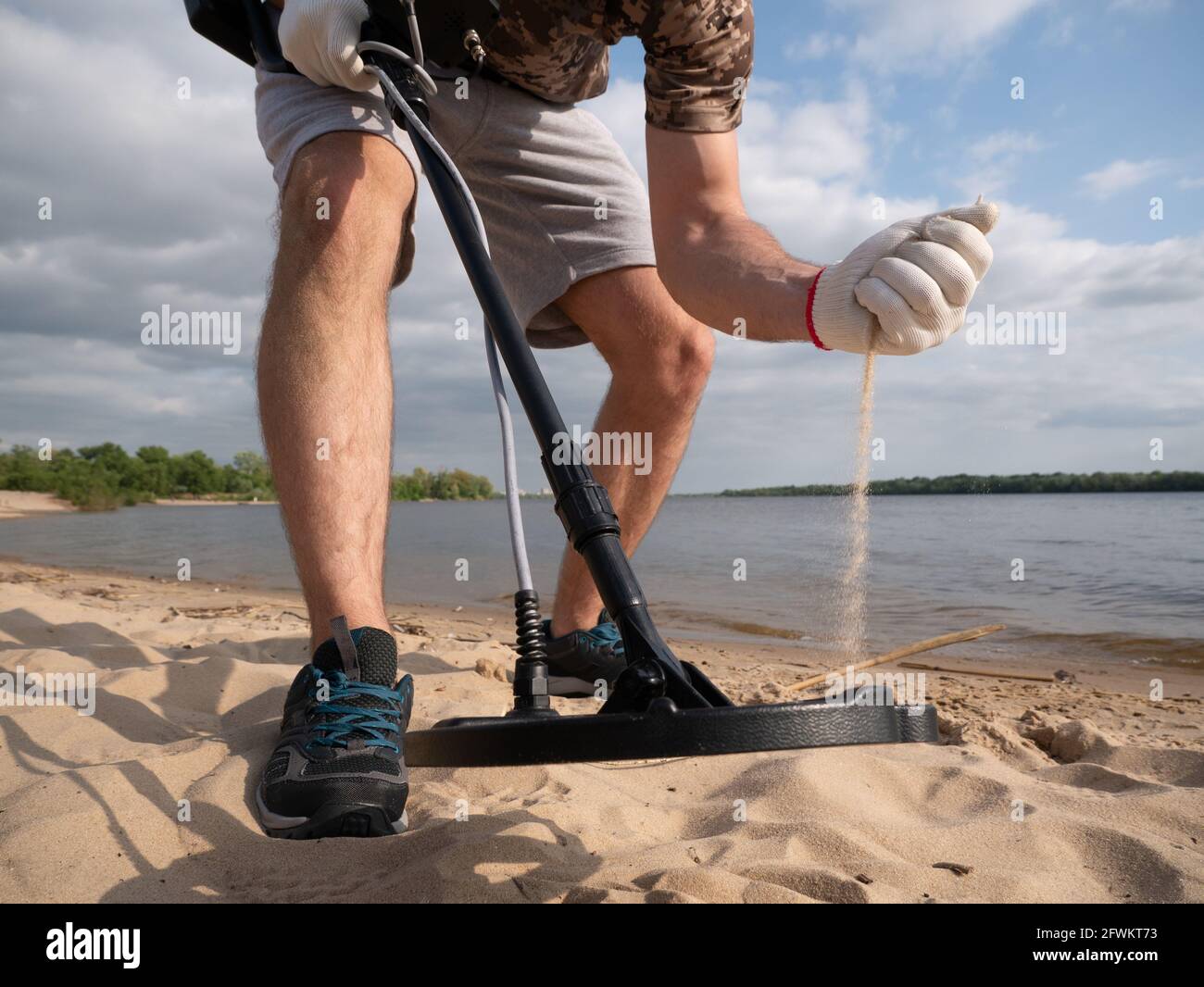 Mann an einer sandigen Küste, der an einem sonnigen Sommertag mit einem Metalldetektor nach einem Schatz sucht. Stockfoto