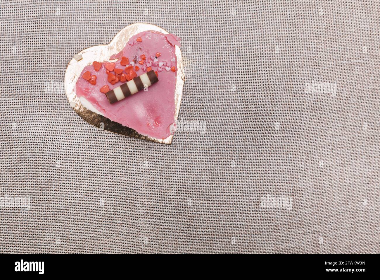 Herzförmiger Erdbeerkuchen, serviert auf einer goldenen Platte zum Valentinstag-Dessert. Es ist mit schwarzen und weißen Schokoladeneklaren und Zuckerrohr geschmückt Stockfoto
