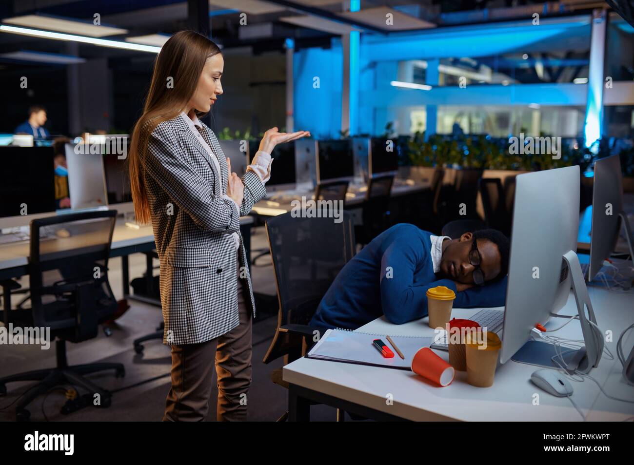 Frau schaut auf den schlafenden Manager, Nachtbüro Stockfoto