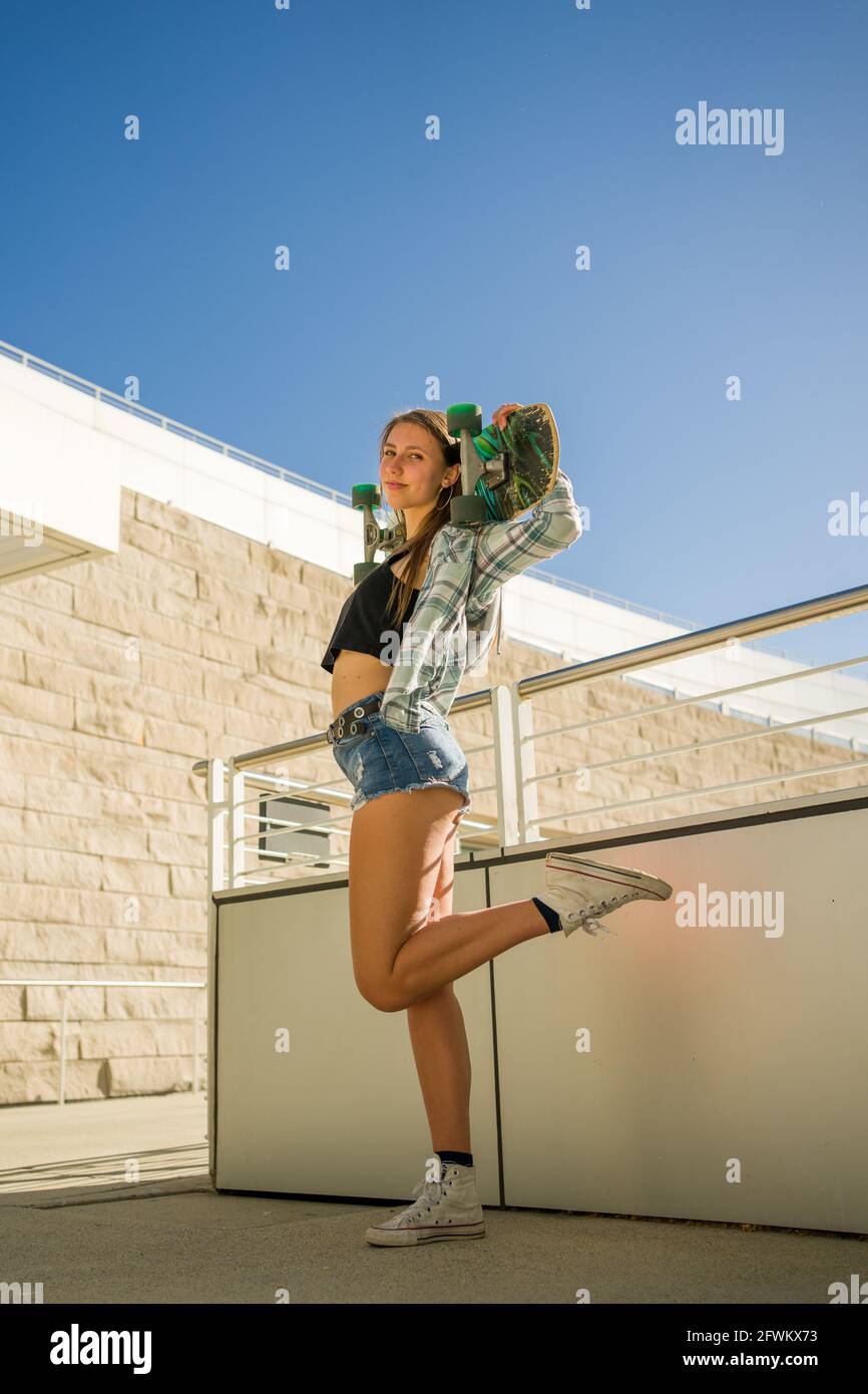 Junge Frau, die ein Skateboard in einer Innenstadtumgebung hält Stockfoto