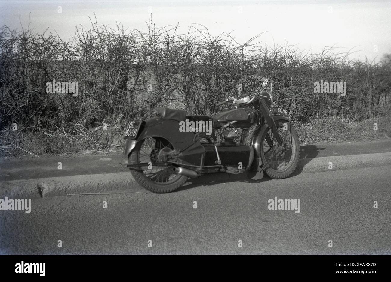 1949, historisches Motorrad der damaligen Zeit, das auf einer Straße neben einem Bürgersteig geparkt war, England, Großbritannien, möglicherweise ein Ex-Militärmotorrad, da es ein Kennzeichen - OC 6088 - auf der Verkleidung über dem Vorderrad angebracht hat. Auch eine Abdeckung oder Verkleidung über dem Motor ist ungewöhnlich. Stockfoto