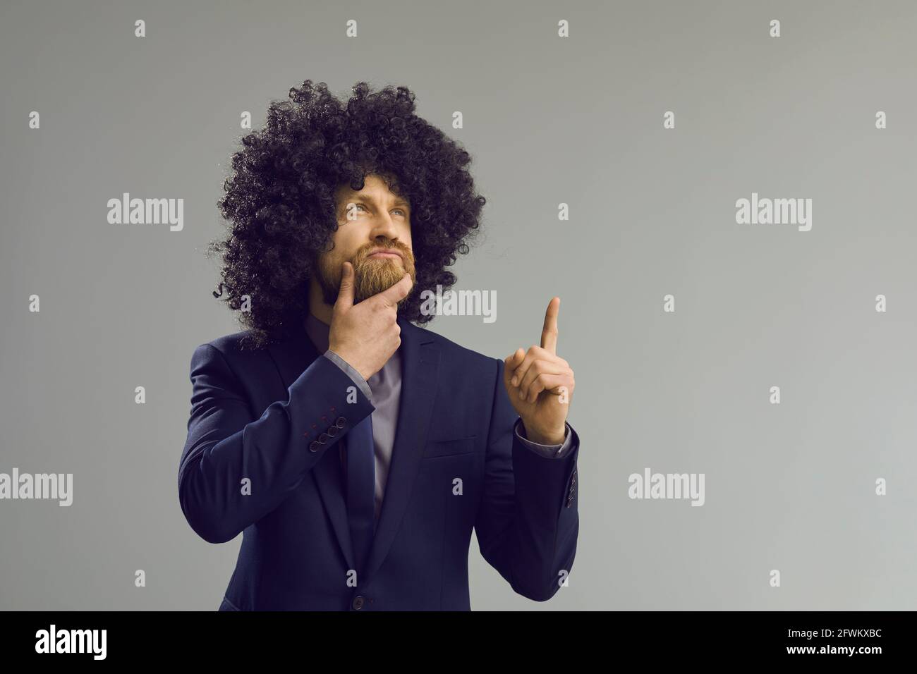 Kaukasischer Hipster-Mann in lustiger lockiger Afro-Haarperücke denkend Und Brainstorming Stockfoto