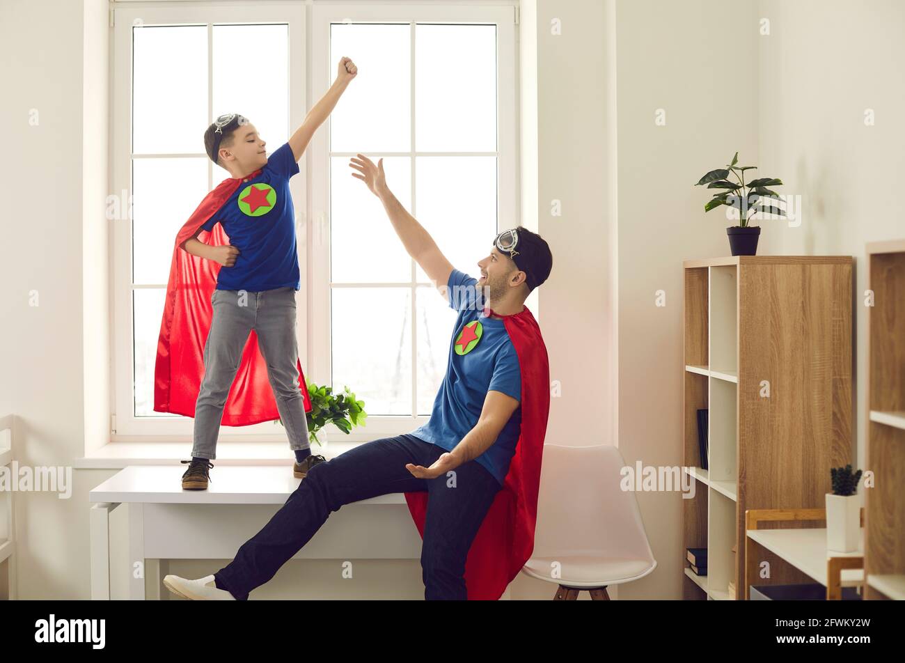 Glückliches, selbstbewusstes Kind und sein Vater kleideten sich als Superhelden beim Spielen Lustige Spiele zu Hause Stockfoto
