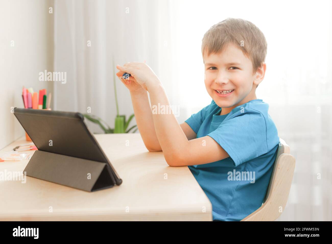 7 Jahre alter Junge, der Unterricht macht und am Schreibtisch in seinem Zimmer sitzt. Glückliches Kind, das zu Hause mit einem Tablet lernt. Fernunterricht und Lernkonzept Stockfoto