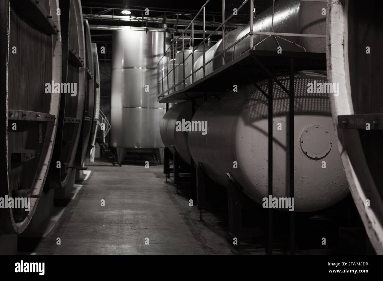Dunkle Holzfässer und Stahltanks befinden sich in einem Keller der Weinkellerei, Nahaufnahme mit selektivem Fokus Stockfoto