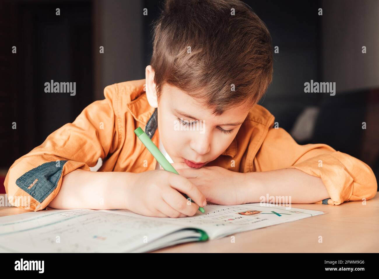 Intelligenter 7 Jahre alter Junge, der Hausaufgaben schreibt und am Schreibtisch sitzt. Kinderschrift im Notizbuch. Nahaufnahme Stockfoto