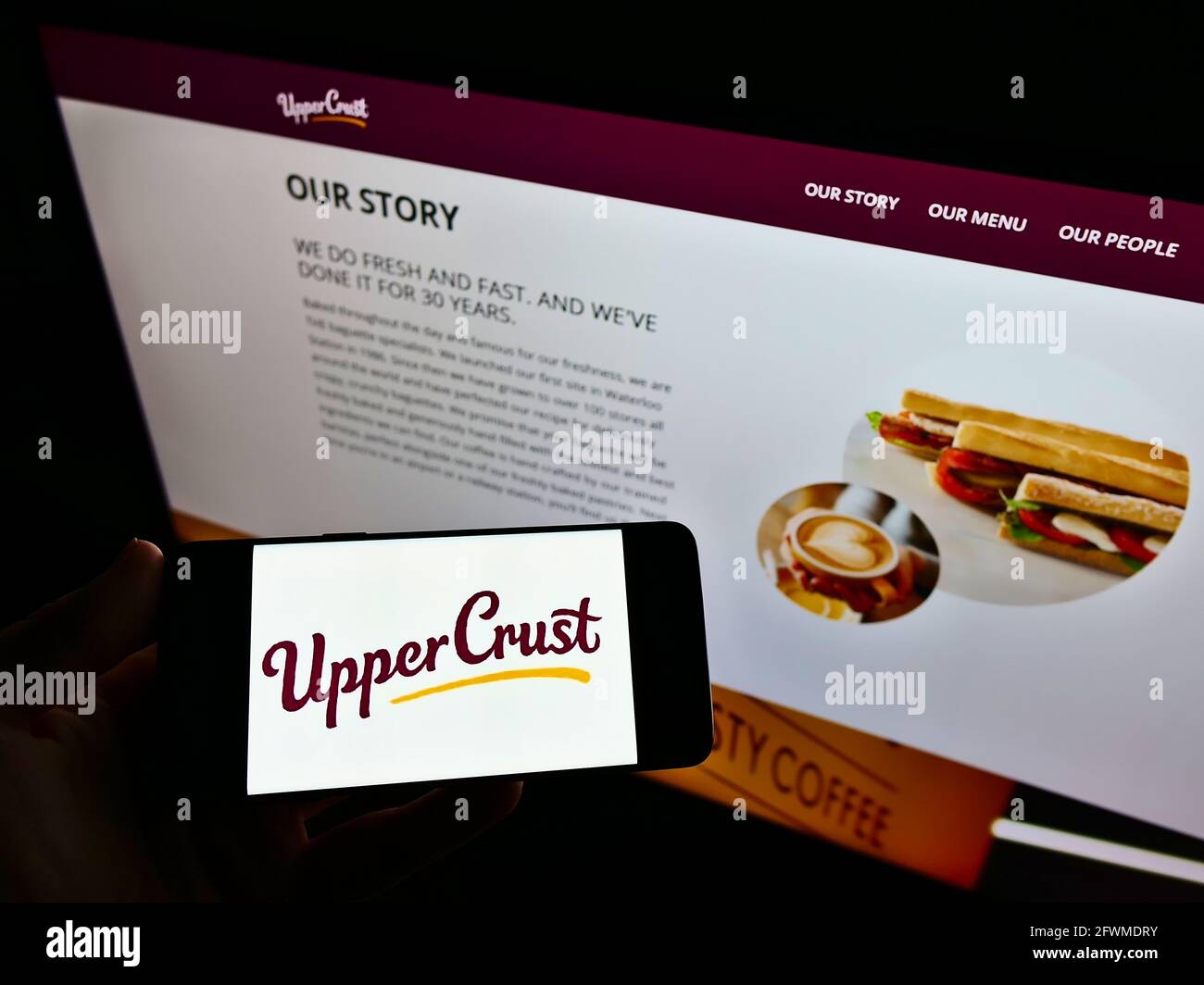 Person mit Mobiltelefon und Business-Logo der Restaurantkette Upper Crust auf dem Bildschirm vor der Webseite. Konzentrieren Sie sich auf die Telefonanzeige. Stockfoto