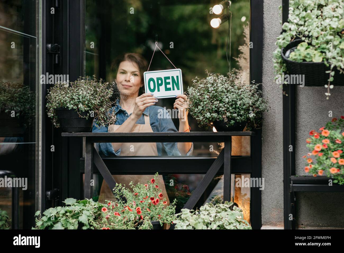 Der Inhaber eines kleinen Unternehmens lächelt, während er ein Schild für die Wiedereröffnung des dreht Ort nach Quarantäne aufgrund von covid-19 Stockfoto