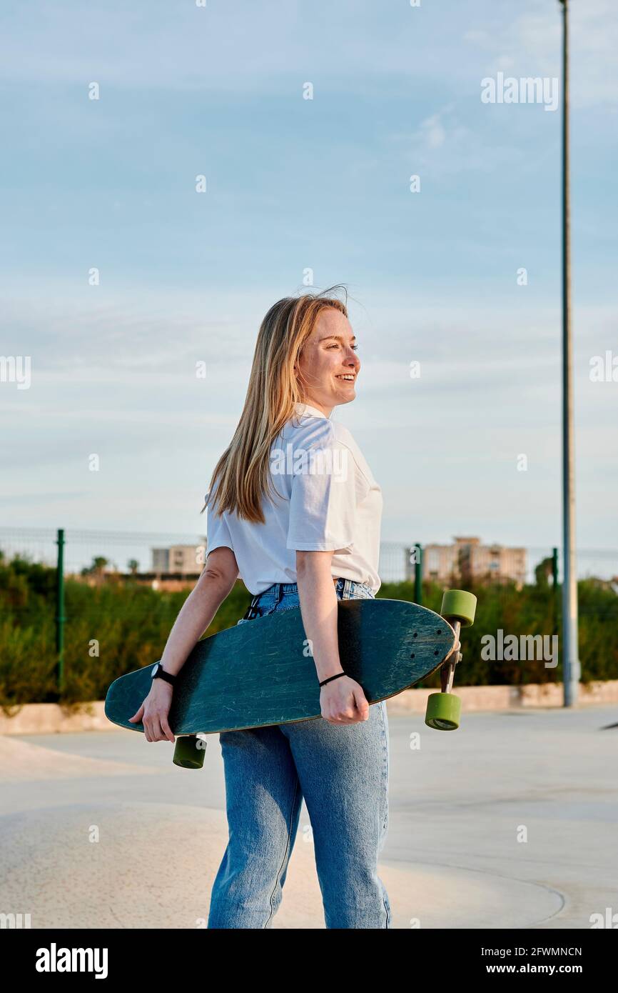 Junge blonde Frau lächelt und hat Spaß mit einem Skateboard Stockfoto