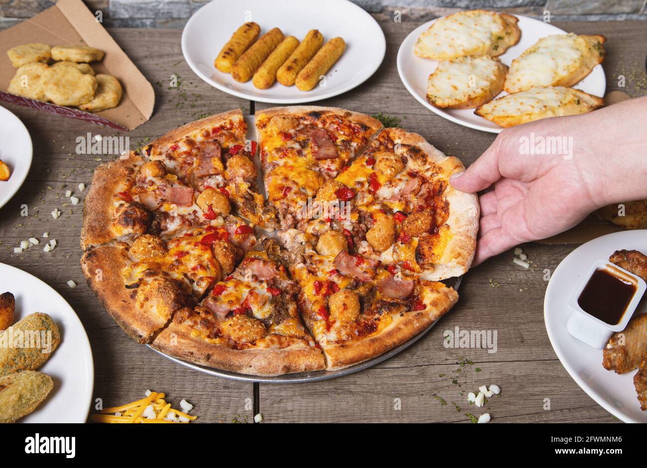 Die Hand des Mannes fängt ein Stück Pizza auf einem Holztisch Stockfoto