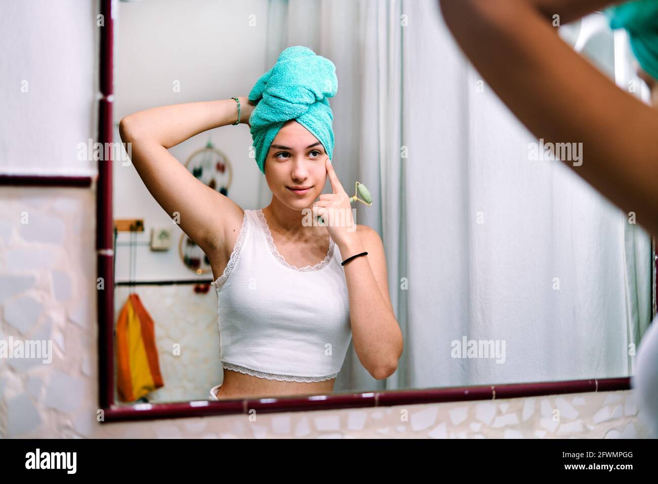Ein junges Mädchen mit einem Handtuch auf dem Kopf macht eine Gesichtsbehandlung Massage im Badezimmer zu Hause Stockfoto