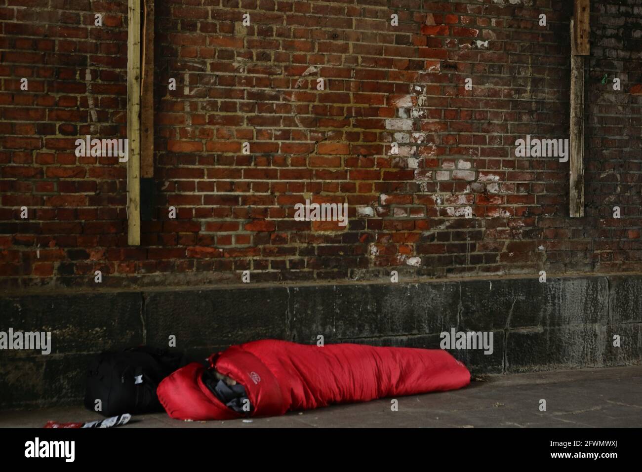 London (UK), 23. Mai 2021: Eine obdachlose Person wird unter einer Brücke gesehen, die in einem roten Schlafsack in der Nähe der Embankment-Station am Südufer schläft. Stockfoto