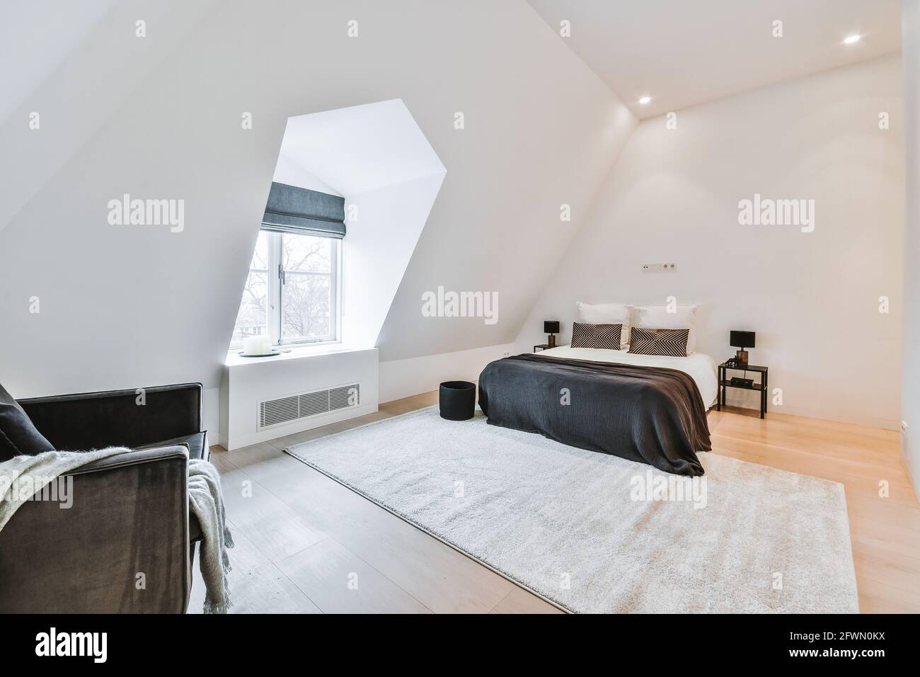 Geräumiges, weißes Schlafzimmer mit großem Bett und Tischen darunter Dachboden mit Teppich und gemütlichem Sessel Stockfoto