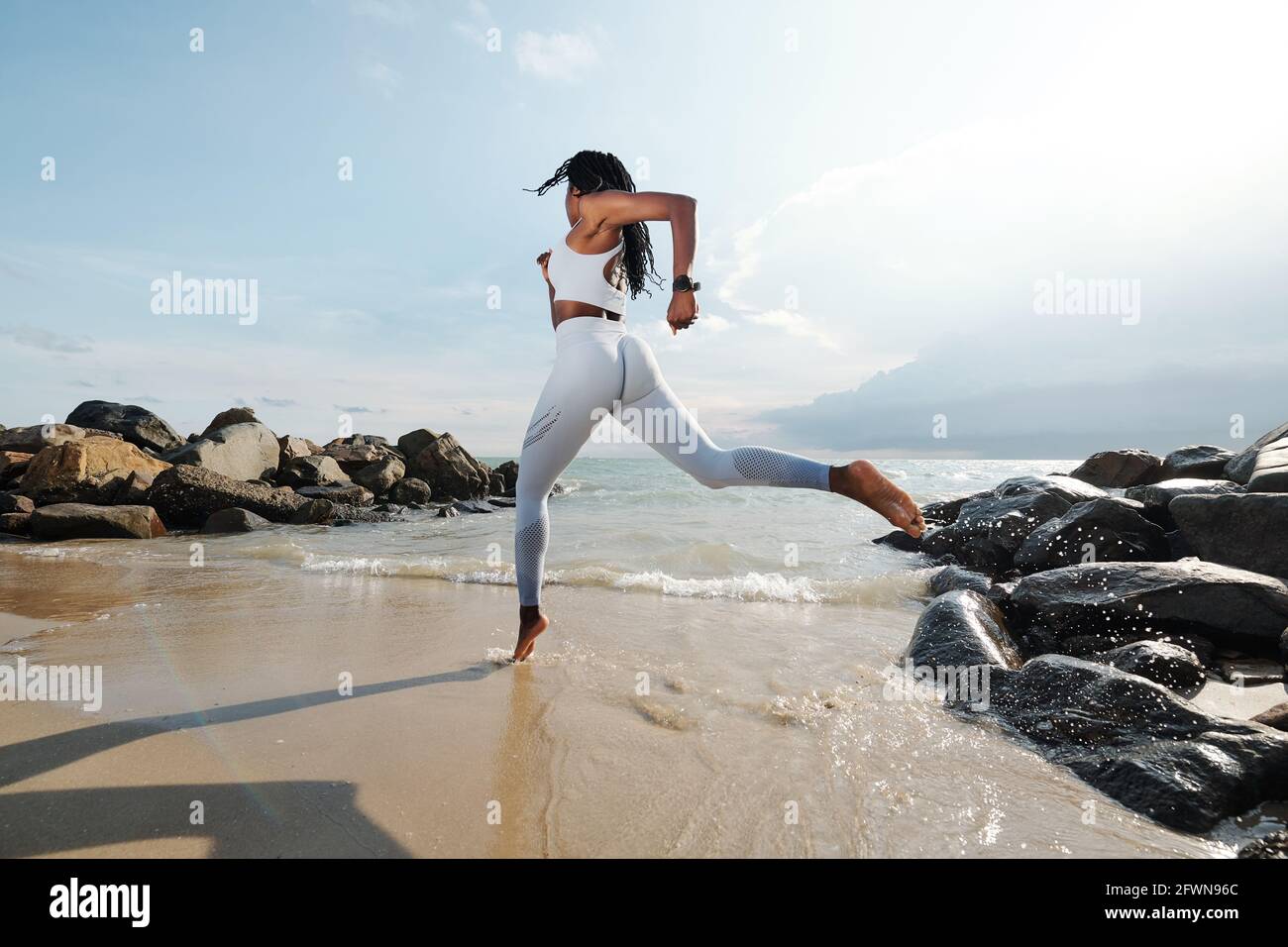 Sportlerin in weißer Sportbekleidung, die am Sandstrand läuft Stockfoto