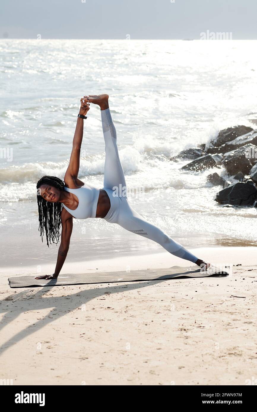 Starke, hübsche Sportlerin, die die Seitenplanke mit angeschraubtem Bein macht Strand am Morgen Stockfoto