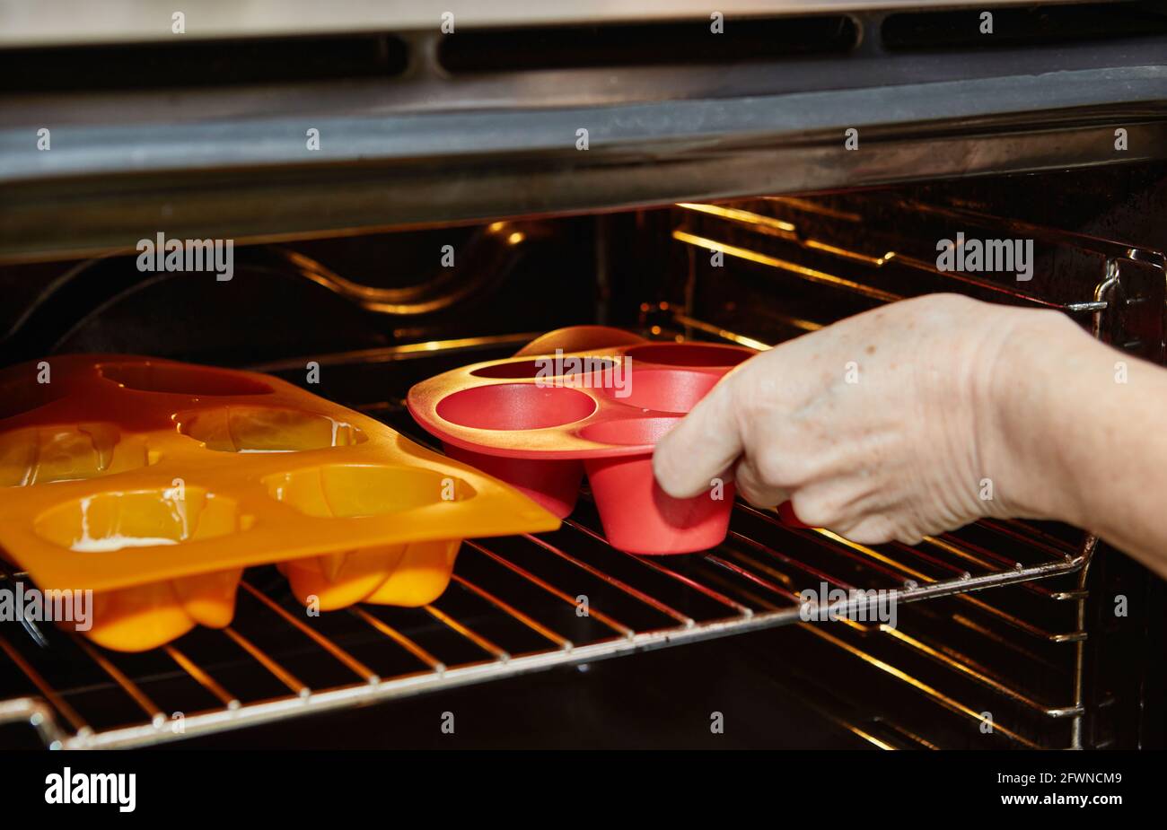 Frau setzt Muffin-Dosen in den Ofen, um sonnengetrocknet zu backen Tomatenmuffins Stockfoto