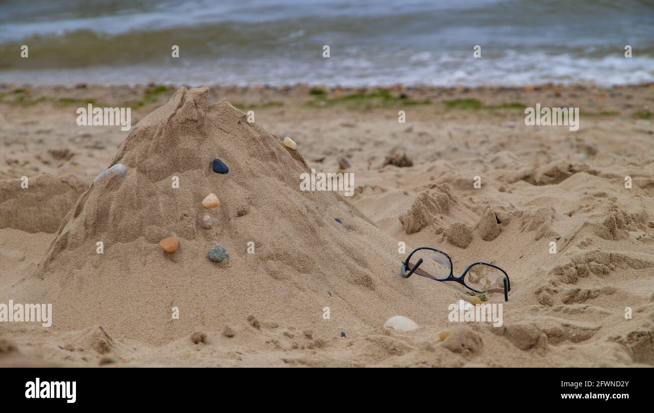 Gläser vergessen auf dem Sand am Strand. Sandburg vor dem Hintergrund des Wassers. Stockfoto