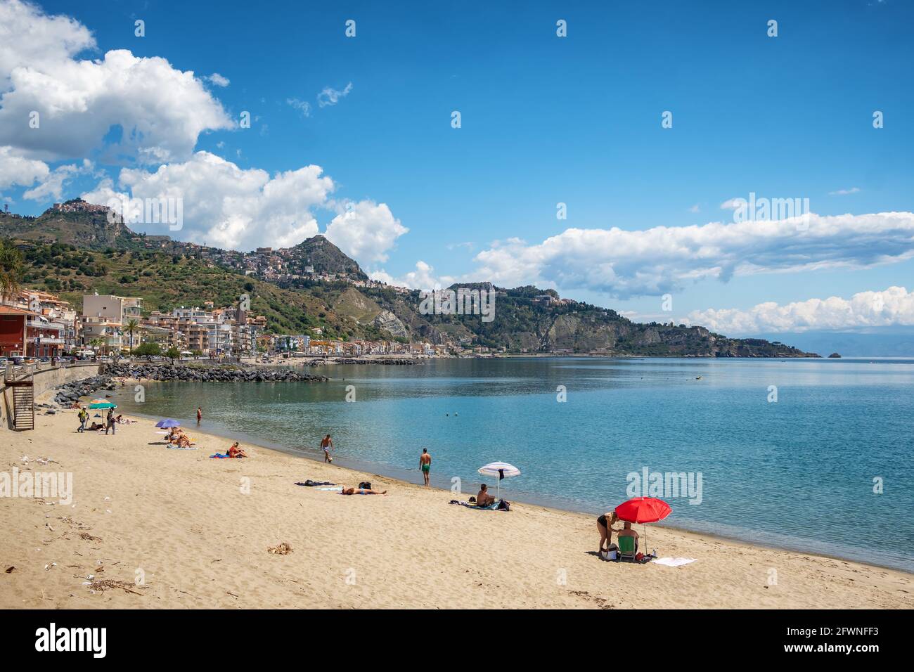 Nicht identifizierte Menschen am Strand in Giardini Naxos mit Taormina Stadt im Hintergrund, Sizilien Stockfoto