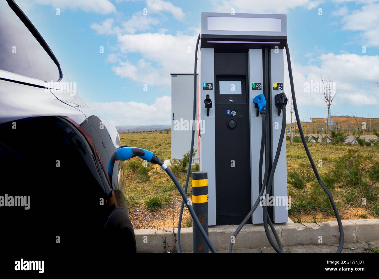 EV-Fahrzeug an Ladegerät und EV-Ladestation angeschlossen. Ladestation für Elektroautos in der Nähe der Autobahn. Elektroauto. Emissionsfreies Aufladen des Fahrzeugs. Kohlenstofffrei Stockfoto