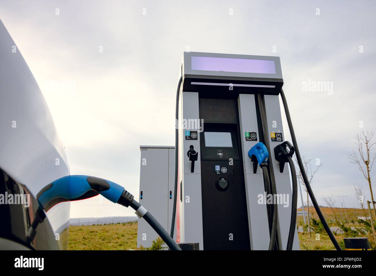 EV-Fahrzeug an Ladegerät und EV-Ladestation angeschlossen. Ladestation für Elektroautos in der Nähe der Autobahn. Elektroauto. Emissionsfreies Aufladen des Fahrzeugs. Kohlenstofffrei Stockfoto