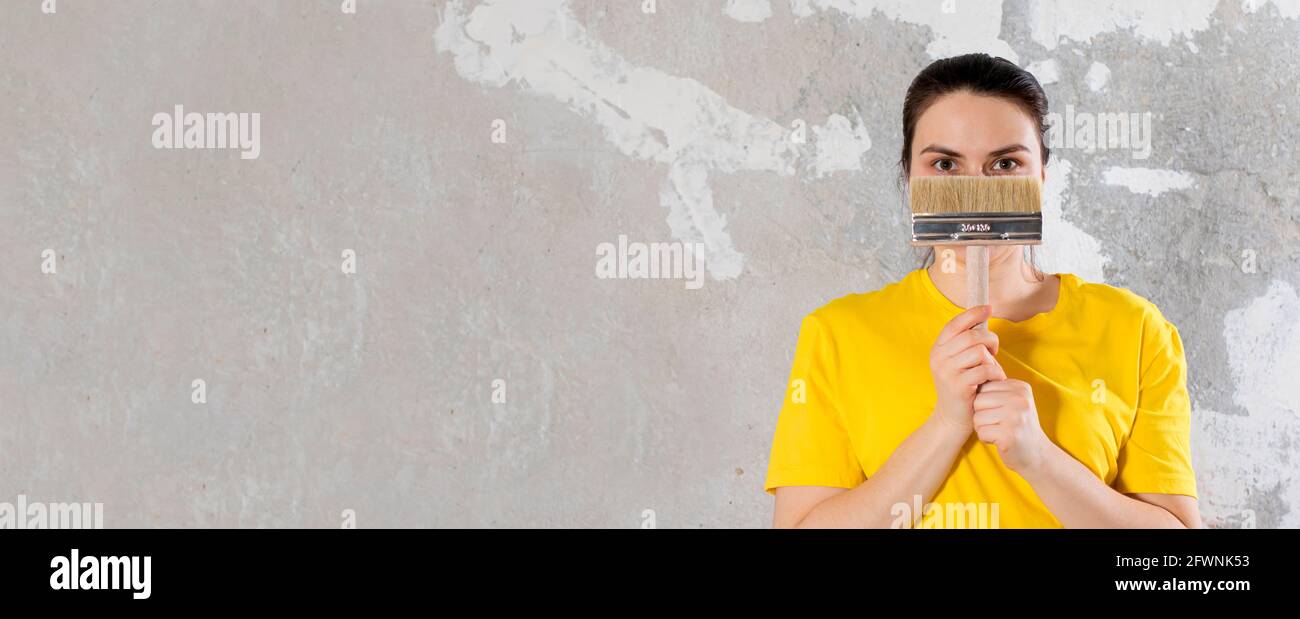 Eine Reparaturfrau in einem gelben, hellen T-Shirt hält einen Pinsel. Für Text platzieren. Schlüsselfertige Reparaturen. Stockfoto