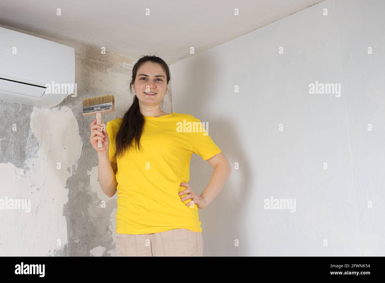 Eine Reparaturfrau klebt weiße Tapeten an der Wand in der Nähe Die Klimaanlage unter der Decke Stockfoto