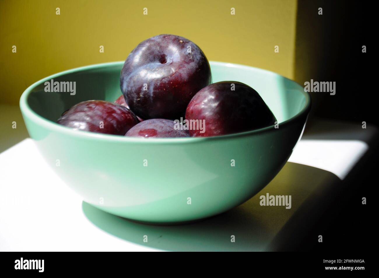 Nahaufnahme einer frischen, reifen Pflaume in einer pastellgrünen Schale auf gelbem Hintergrund Stockfoto