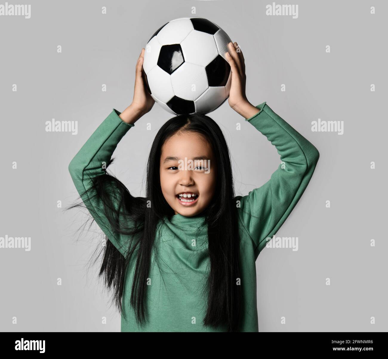 Junge schöne asiatische Mädchen hält Fußball-Fußball über ihren Kopf auf grauem Hintergrund. Happy koreanischen Fußballspieler Kind Stockfoto