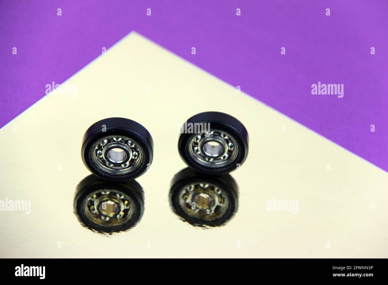 Gruppe von zwei Kugellagern und Zahnrädern schließen auf schönem silbernen Hintergrund mit Reflexionen, und farbigen Papierblättern, starke Farben. Stockfoto