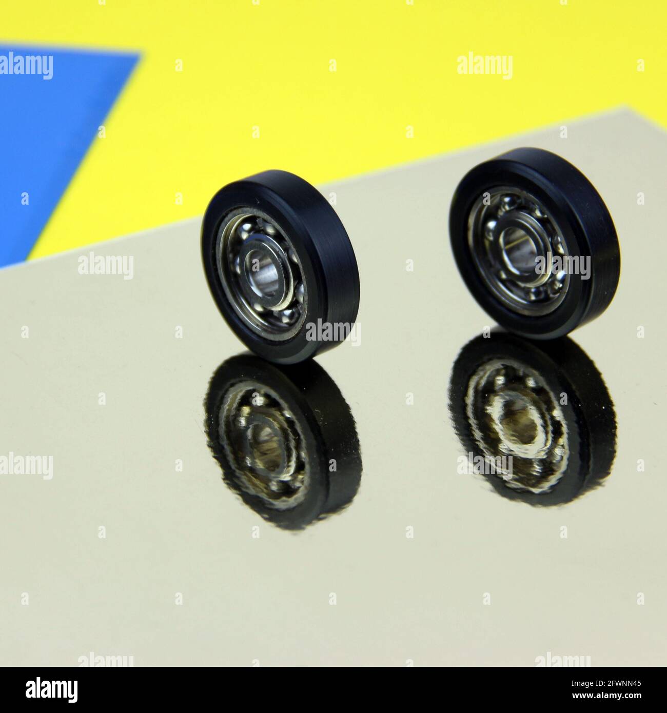 Gruppe von zwei Kugellagern und Zahnrädern schließen auf schönem silbernen Hintergrund mit Reflexionen, und farbigen Papierblättern, starke Farben. Quadratische Zusammensetzung. Stockfoto