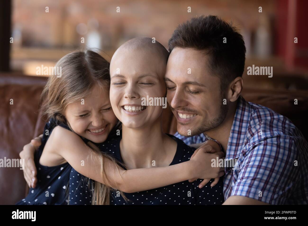 Glückliche Tochter Kind und Vater umarmt krank haarlose Mutter Stockfoto