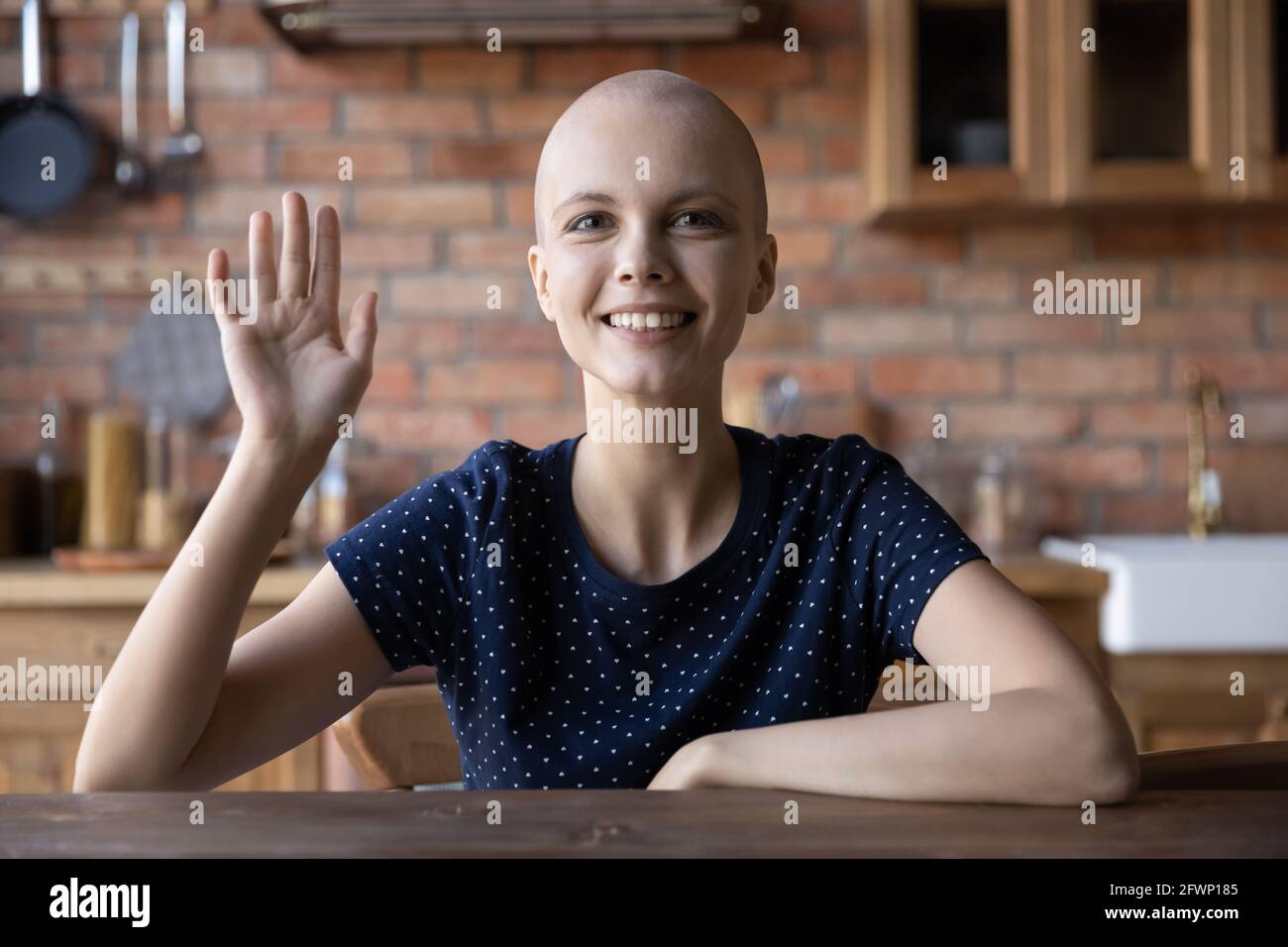 Glückliches haarloses Mädchen mit Krebs lächelnd, schauend und winkende Hand Stockfoto
