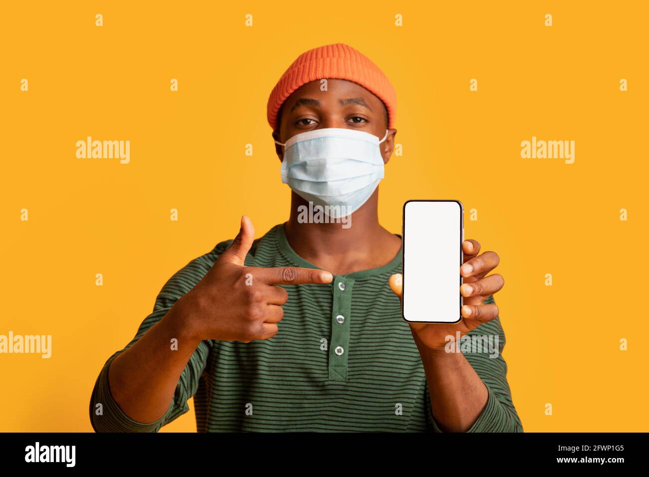 Junger schwarzer Mann in medizinischer Maske zeigt auf Smartphone mit Weißer Bildschirm Stockfoto