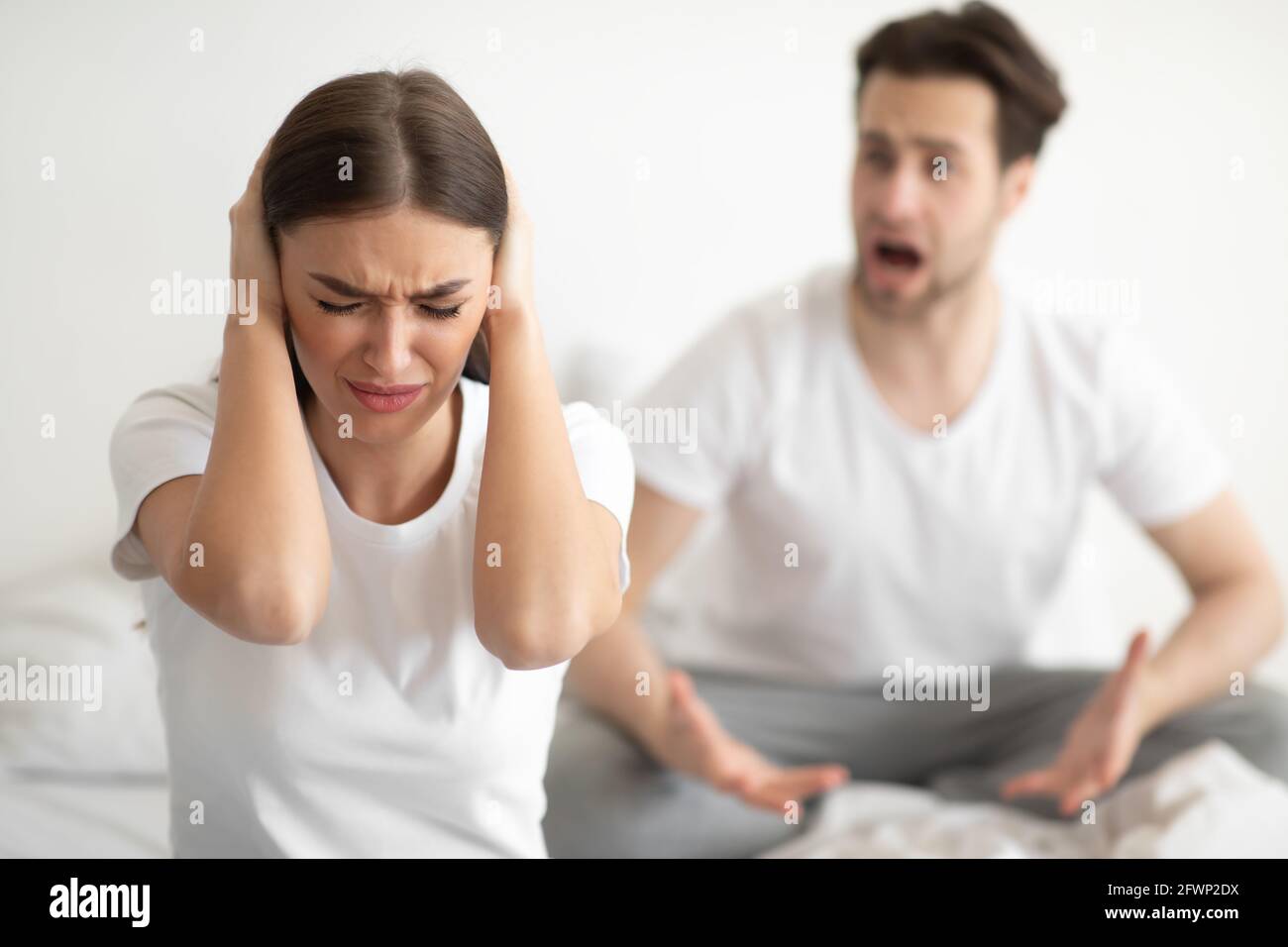Unglückliche Frau, Die Ohren Bedeckt, Während Verärgerlicher Ehemann Im Schlafzimmer Schrie Stockfoto