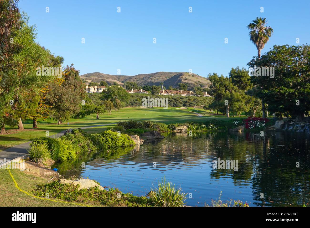 Der von Bäumen gesäumte See auf dem Golfplatz von San Juan Hills mit Hügeln und Wohnhäusern im Hintergrund von San Juan Capistrano. Kalifornien, USA Stockfoto