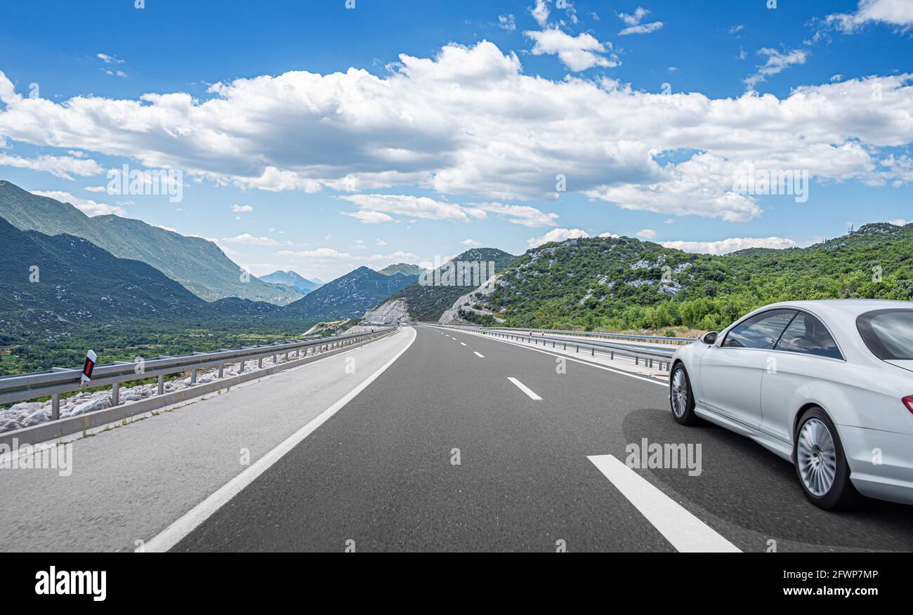 Weißes Auto fährt die Straße entlang durch den Wald entlang der Autobahn. Stockfoto