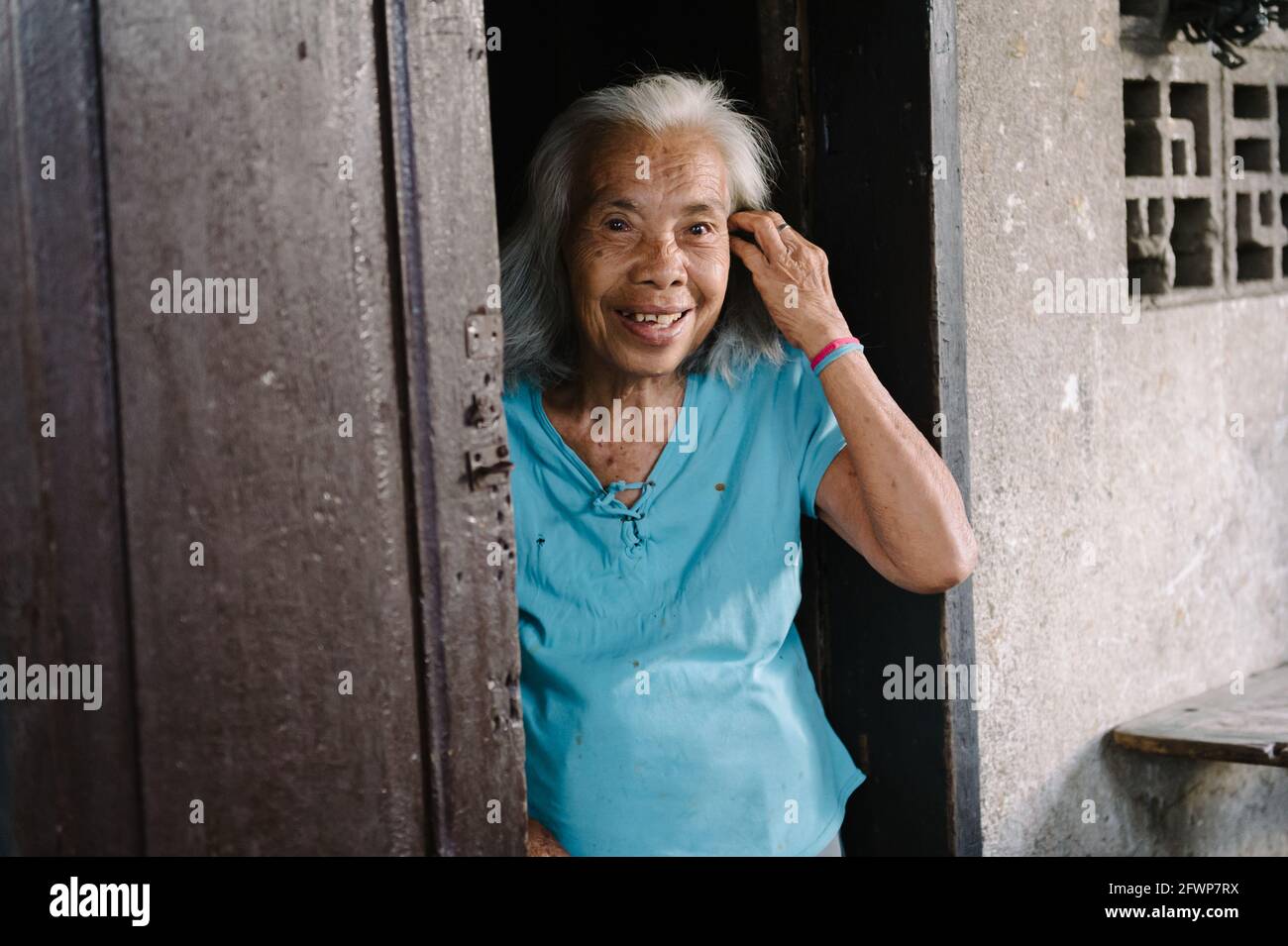 Porträt einer alten asiatischen Dame, die vor ihrer Türschwelle steht und fröhlich zur Kamera lächelt. Stockfoto