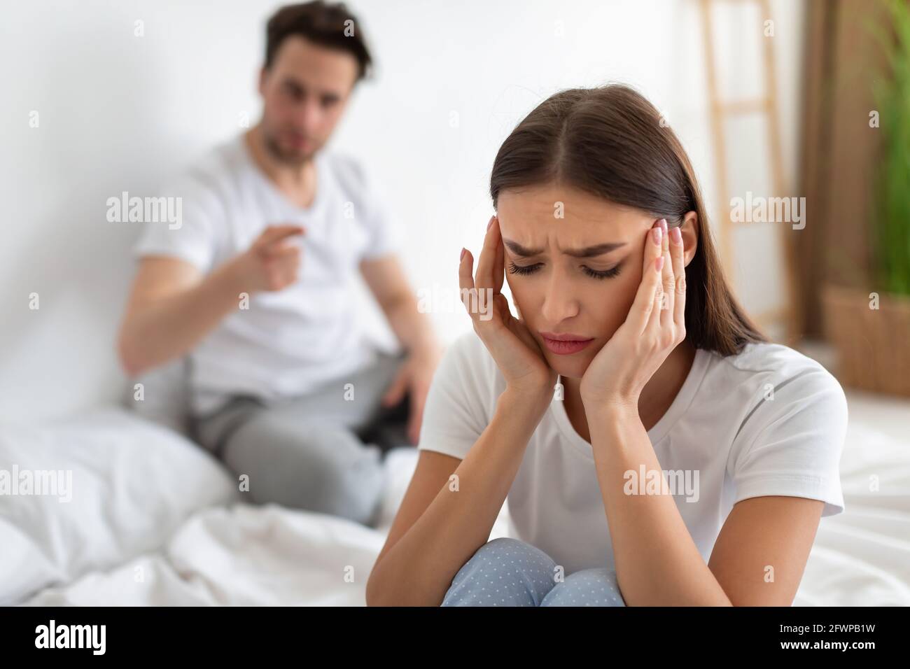 Frau, die den Anschuldigungen des Ehemanns zuhohl, nachdem sie im Schlafzimmer gesessen hatte Stockfoto