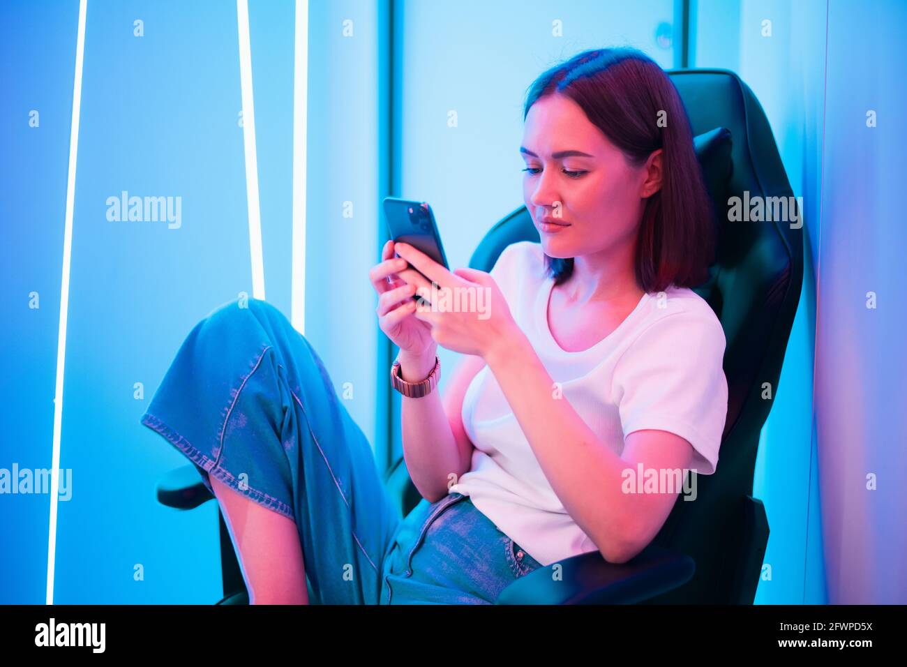Cybersport Gamer spielen mobile Spiel auf dem Smartphone sitzen Auf einem Spielstuhl im neonfarbenen Raum Stockfoto