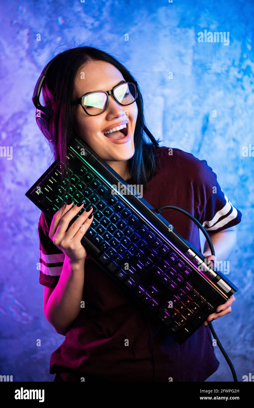 Weibliche eSports Gamer posiert mit einer Gaming-Ausrüstung in Neonlicht. Streamer Mädchen mit einer Gaming-Tastatur stehen Stockfoto