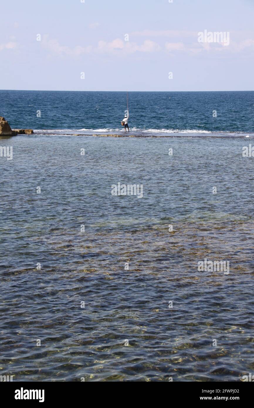 fischer, der im flachen Wasser steht, um seine Angelrute abzuwerfen Stockfoto