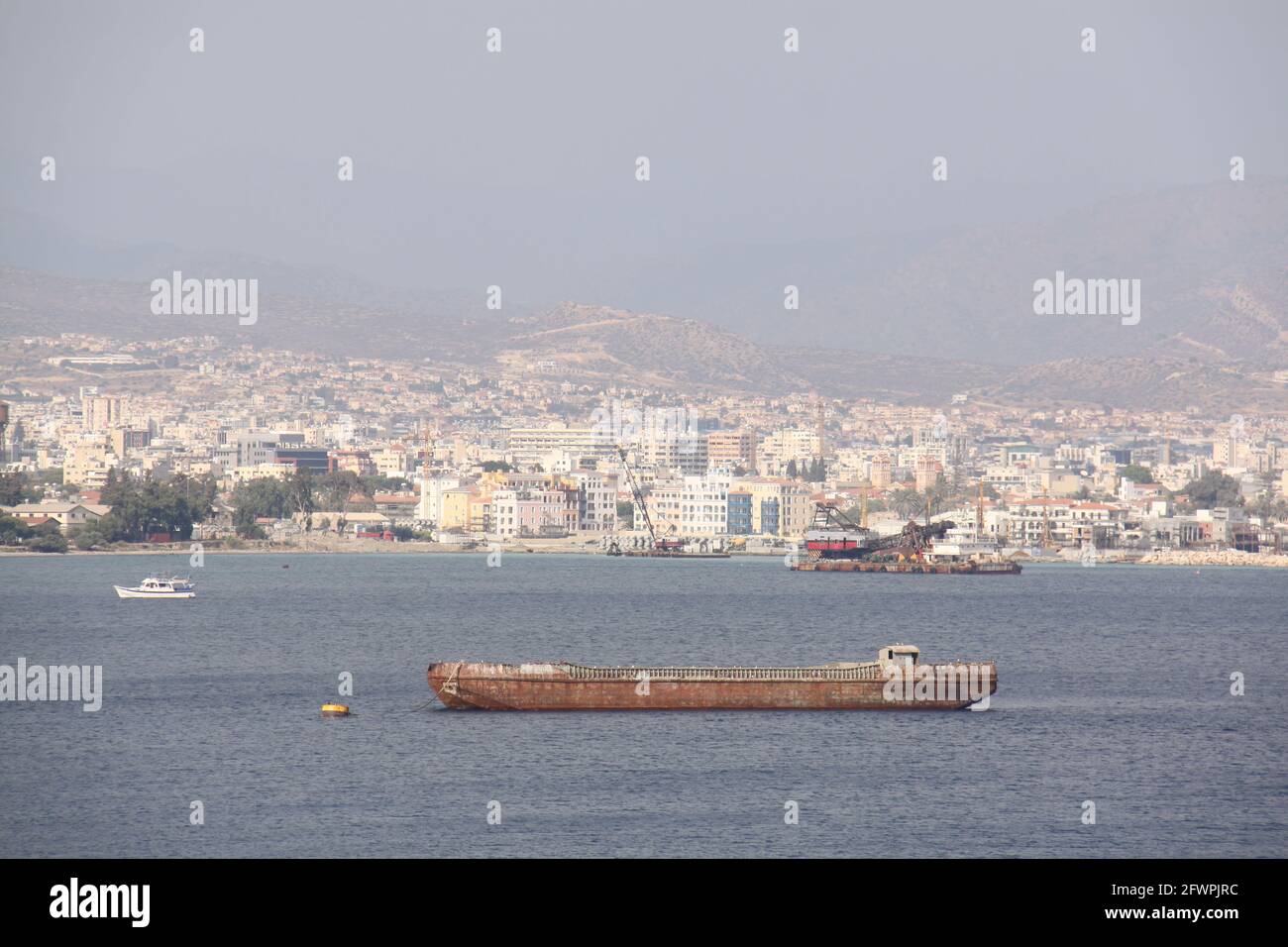 Rostiges altes Schiff, das in der Bucht vor Anker liegt, mit der Stadt am Berghang im Hintergrund Stockfoto