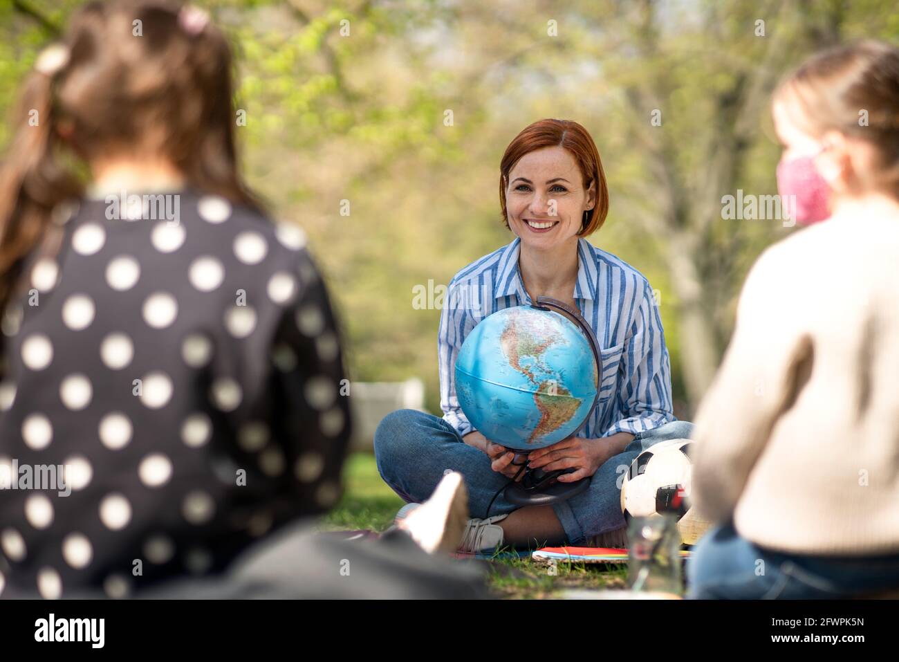 Lehrer mit kleinen Kindern sitzen im Freien im Stadtpark, Lerngruppe Bildungskonzept. Stockfoto