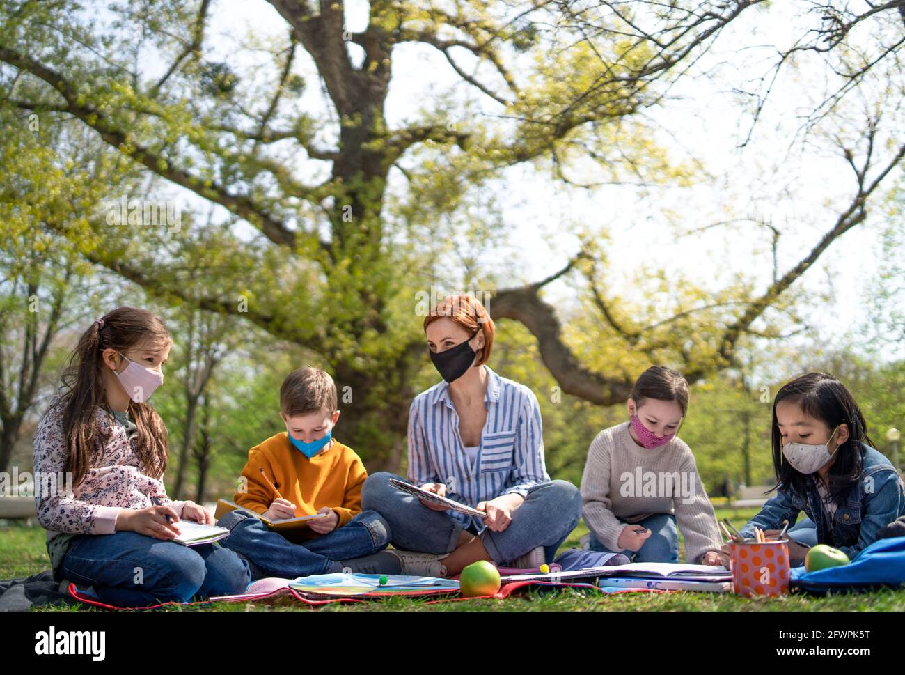 Lehrer mit kleinen Kindern, die im Stadtpark sitzen, lernen Gruppenbildung und Coronavirus-Konzept. Stockfoto