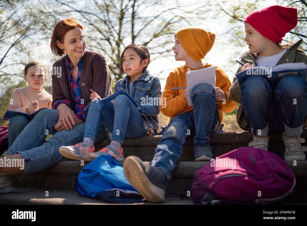 Lehrer mit kleinen Kindern sitzen im Freien im Stadtpark, Lerngruppe Bildungskonzept. Stockfoto
